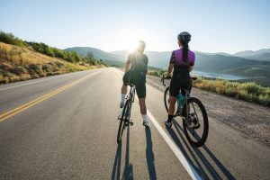 Two female cyclists looking towards the sun with a long scenic road ahead of them.